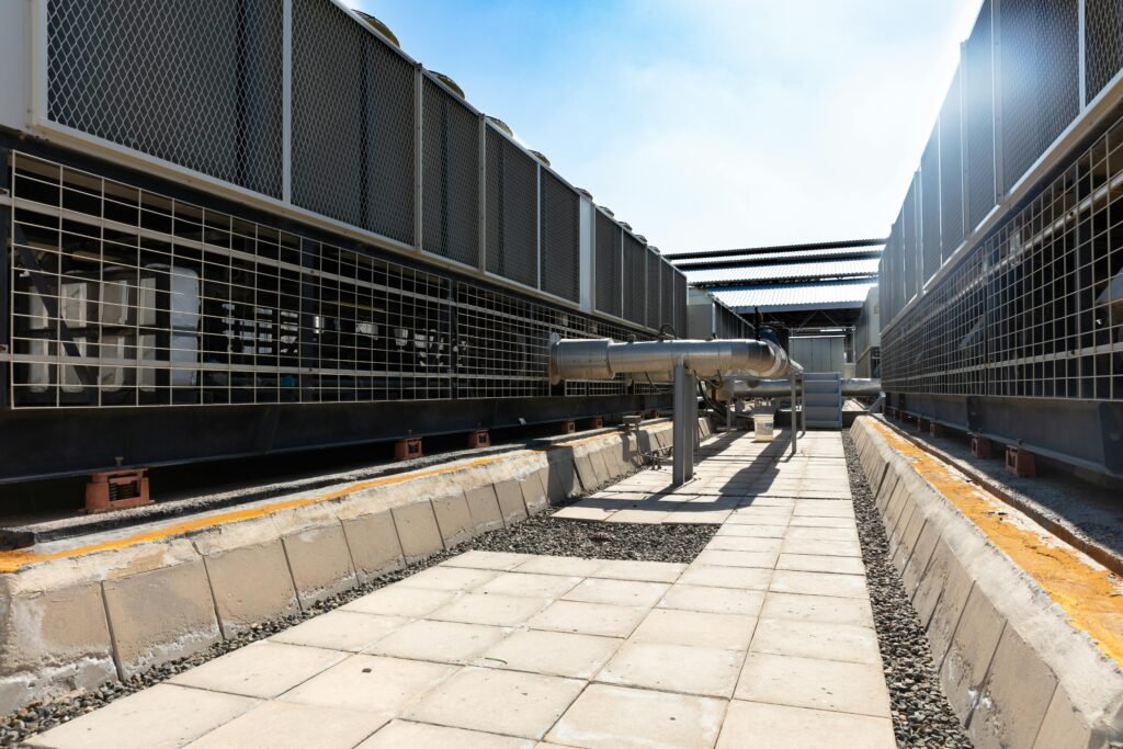 Detailed view of an industrial cooling system with metal pipes and sunlit concrete path.