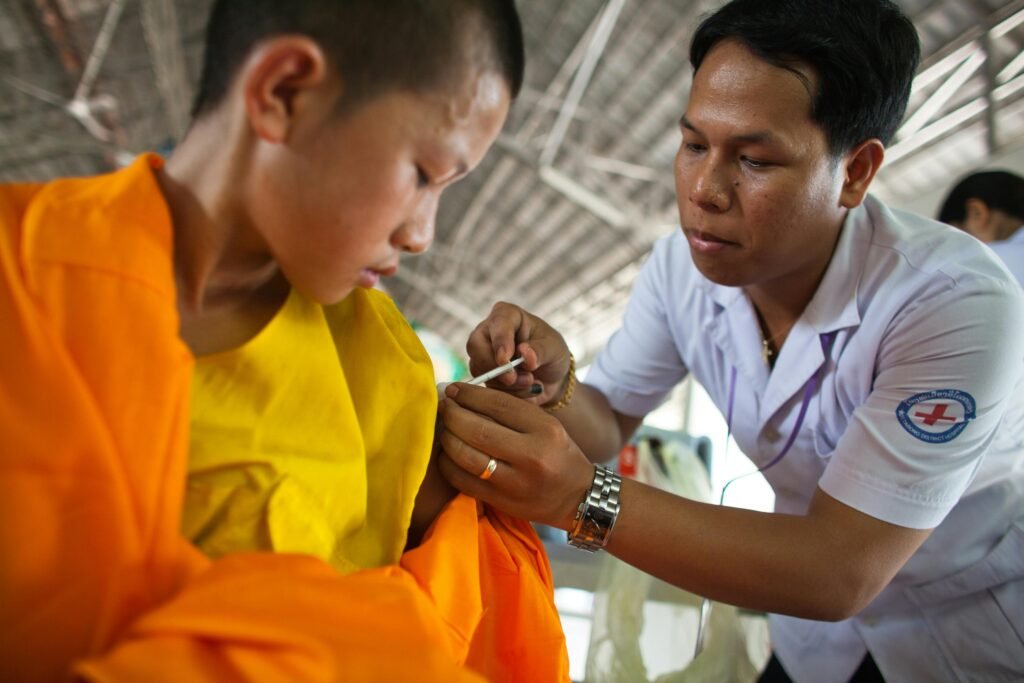 A healthcare worker vaccinates a young boy wearing an orange robe indoors.