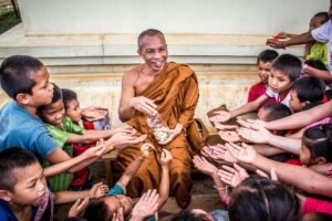 Smiling monk shares food with eager children in an Asian community gathering.